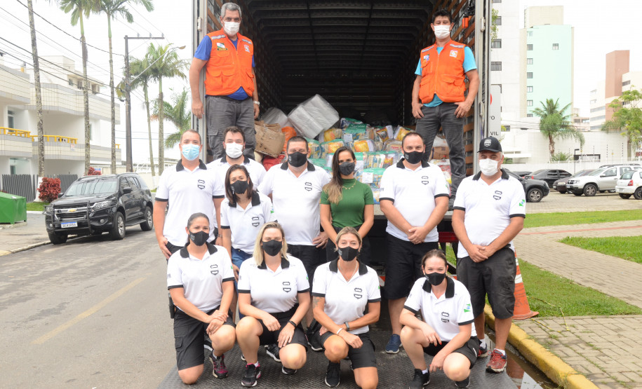 Policiais civis e servidores da Defesa Civil posando para foto junto a caminhao com produtos arrecadados