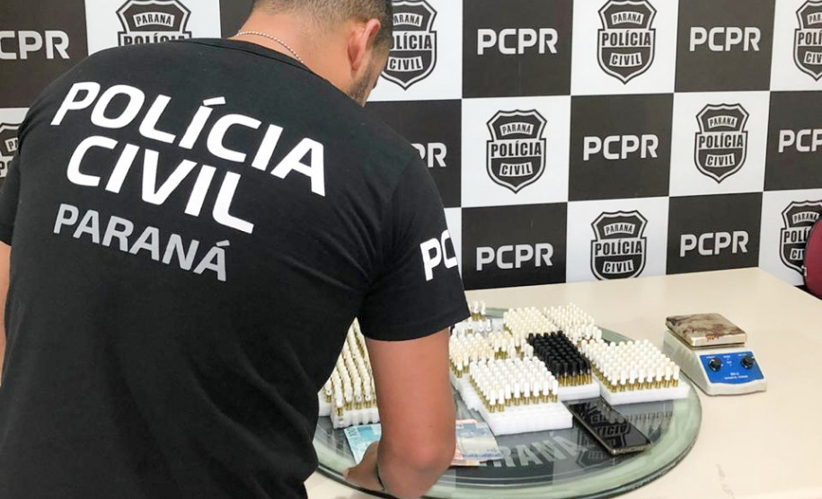Policial civil de costas, organizando sobre uma mesa o material apreendido