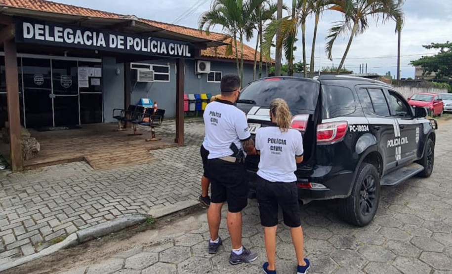 Policiais civis fechando tampa do porta-malas de viatura, em frente à delegacia