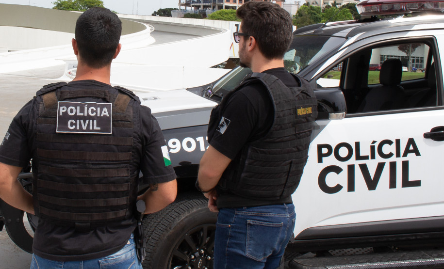 Dois policiais civis ao lado de viatura