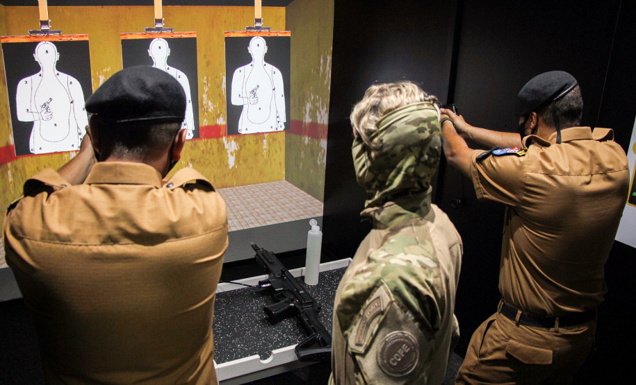 Dois policiais militares apontando as armas para tela de simulador da polícia civil