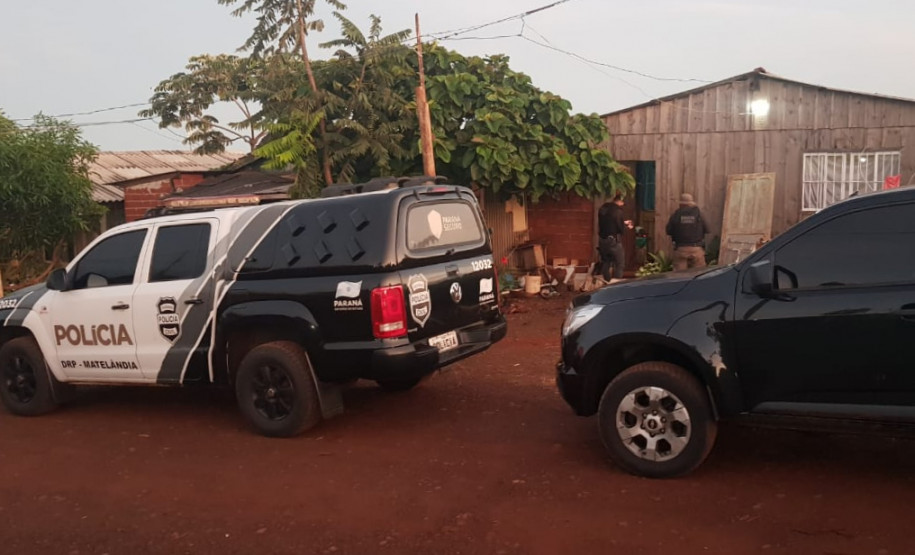 Policiais civis investigando local. Em frente à casa, uma viatura