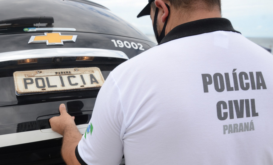 Policial civil fechando tampa de porta-malas de viatura