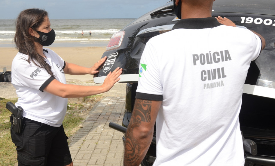 Policiais civis fechando tampa de porta-malas de viatura