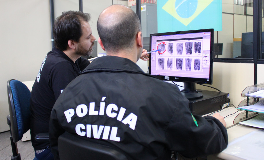 Policiais analisam digitais em monitor