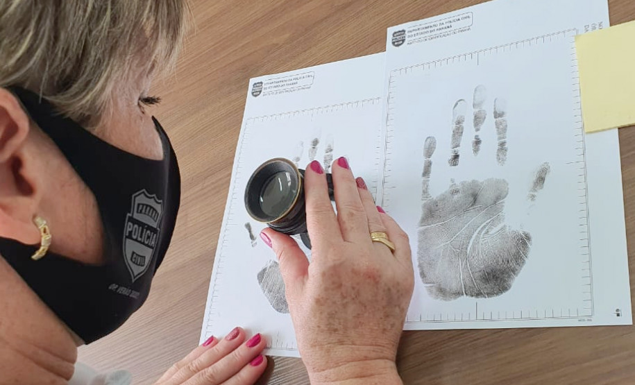 Papiloscopista analisa digital com uma lupa