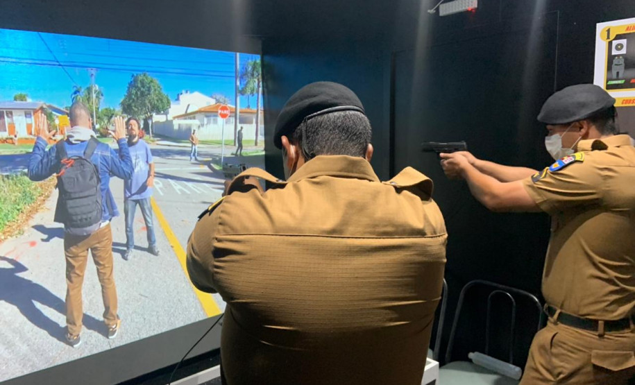 Dois policiais militares apontando as armas para tela de simulador da polícia civil