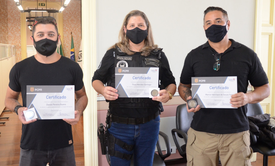 Três ganhadores do concurso posam para foto mostrando certificados e medalha