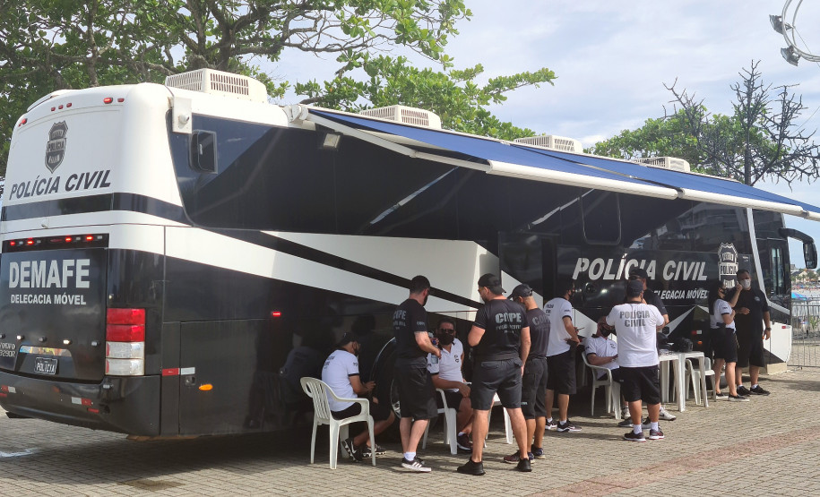 Diversos policiais civis reunidos ao lado do ônibus com a delegacia móvel