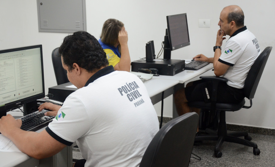 Dois policiais civis. Um deles atendendo veranista na delegacia