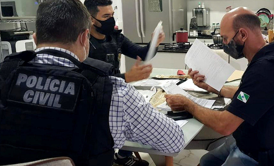 Três policiais civis à mesa, analisando documentos