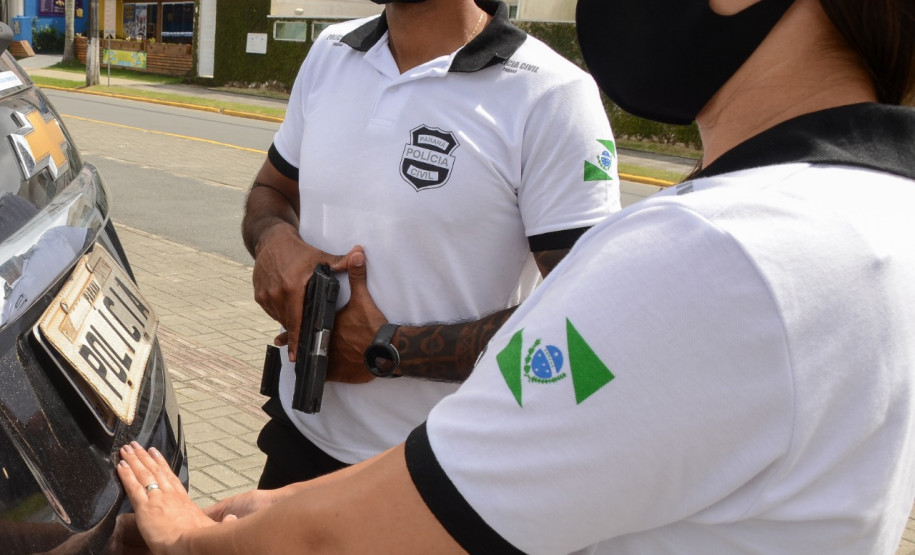Policiais civis com arma próximos à viatura