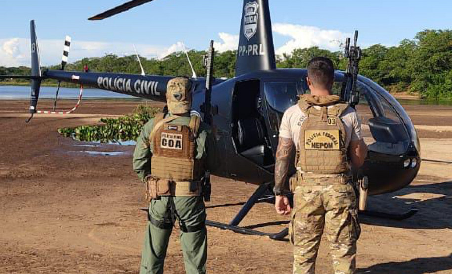 Policiais de costas, ao lado de helicóptero da polícia civil