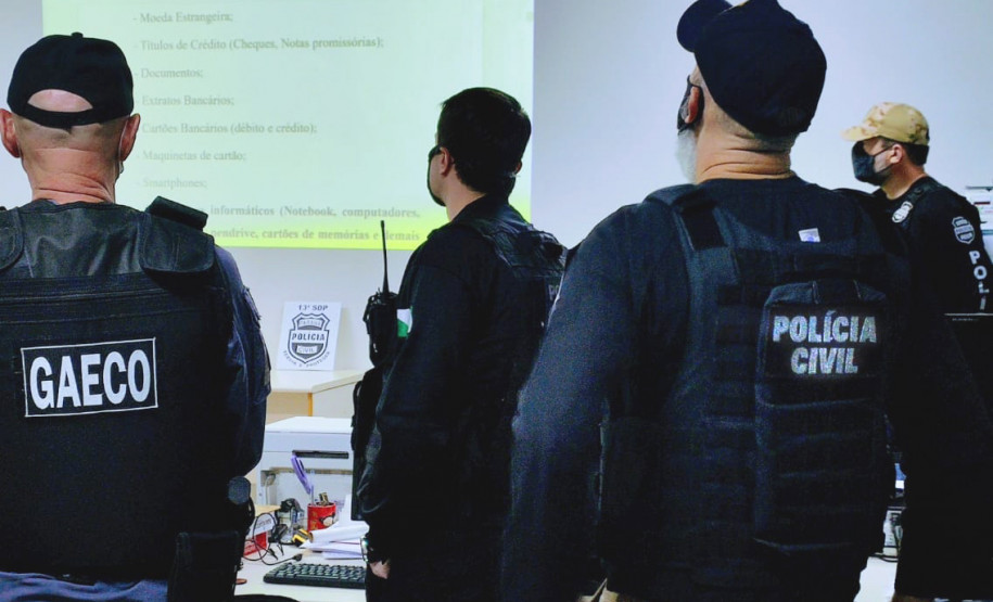 Policiais de costas observam apresentação de slides com dados da operação
