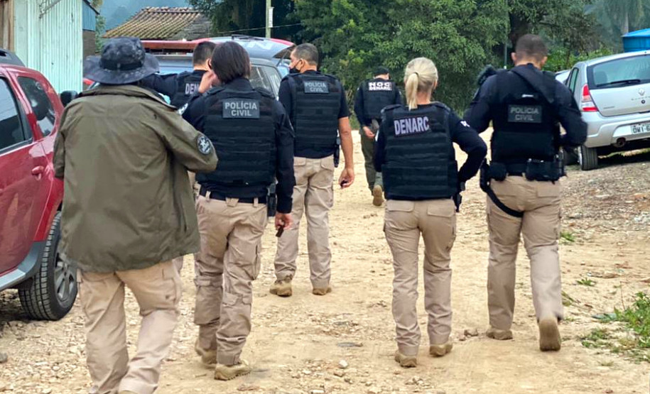 Policiais civis de costas, andando em rua sem asfalto