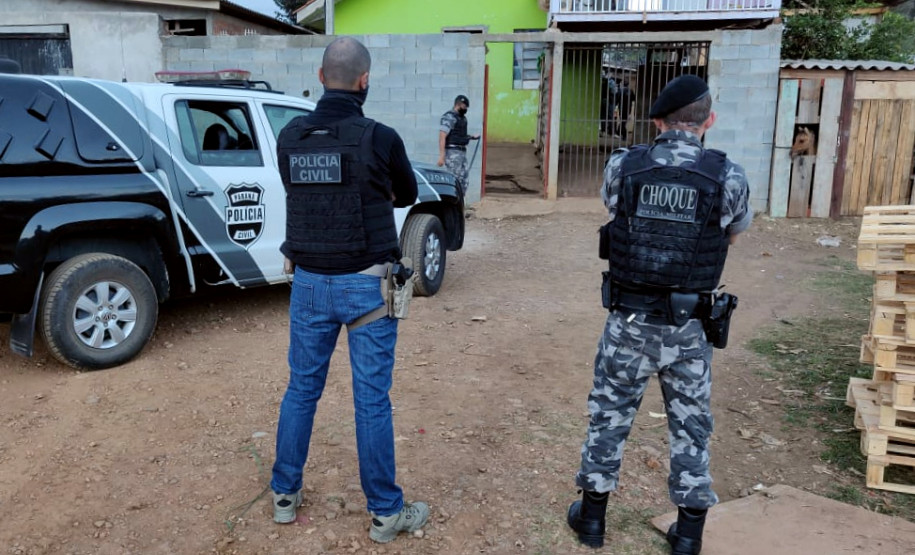 Policiais de costas, ao lado de viatura da polícia civil