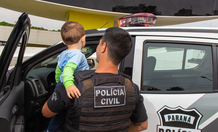 Policial civil aparece com criança no colo ao lado de viatura.