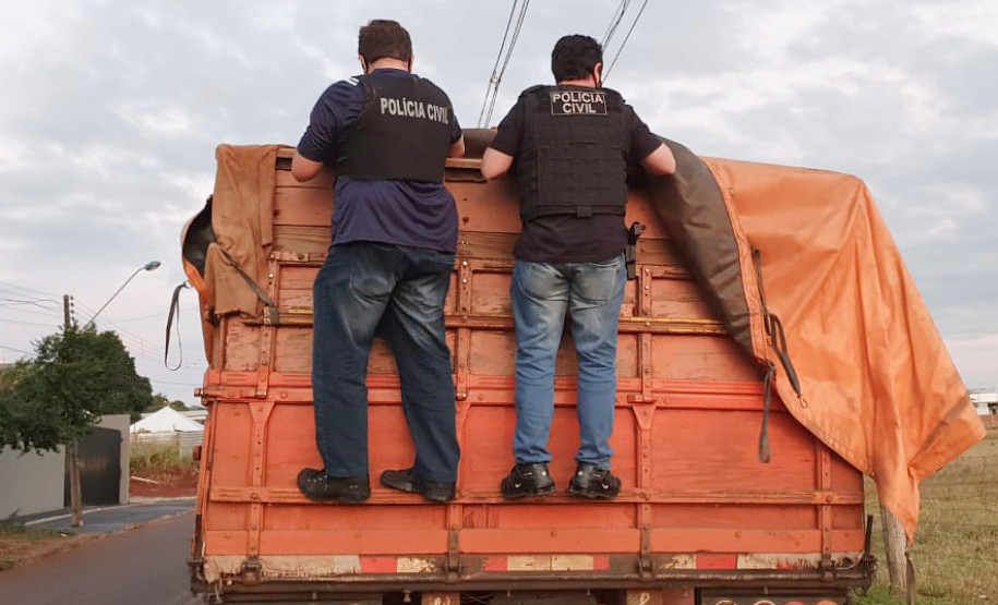 Dois policiais civis na carroceria do caminhão, verificando carga