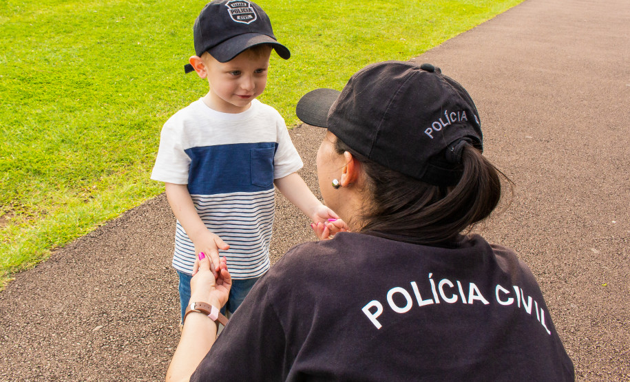Policial civil interage com uma criança, ambos com bonés da polícia