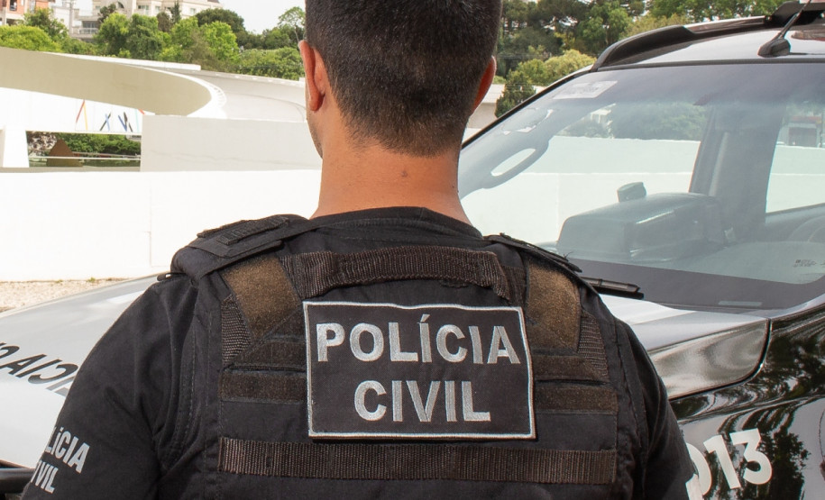 Policial civil de costas, ao lado de viatura