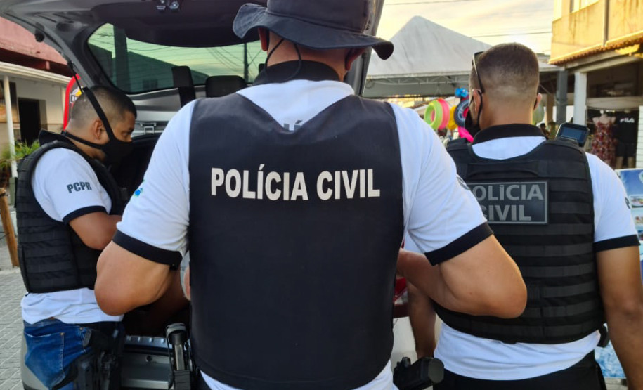 Tres policiais civis ao lado de viatura