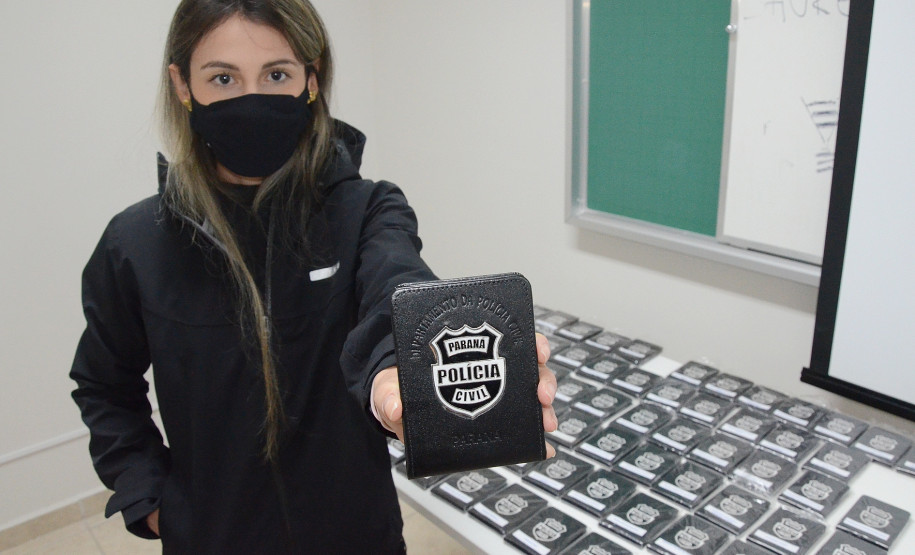 Aluna mostra carteira funcional. Ao fundo, diversas carteiras funcionais agrupadas sobre uma mesa