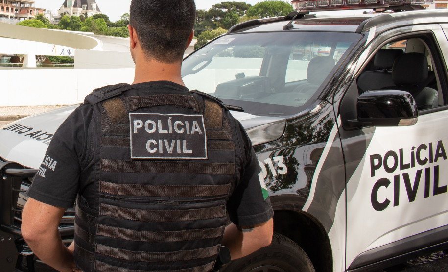 Policial civil de costas, ao lado de viatura