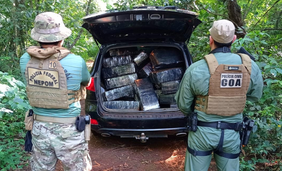 Policiais de costas ao lado de viatura