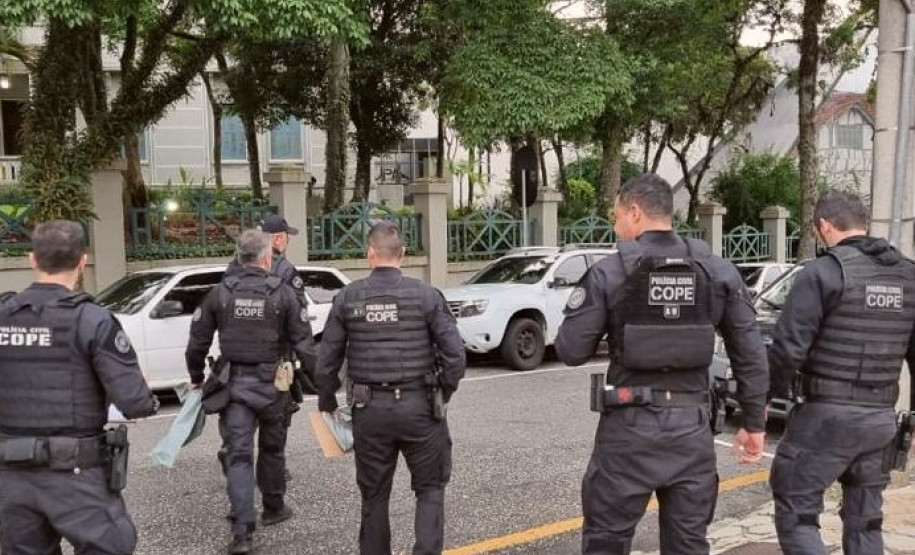 Seis policiais civis de costas, atravessando a rua