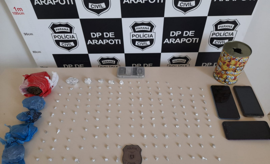 Droga apreendida sobre uma mesa. Ao fundo, banner da polícia civil.