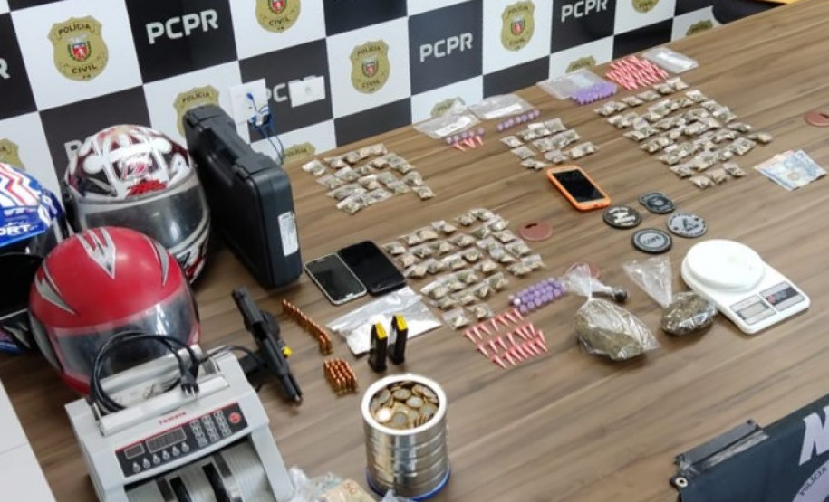 Material apreendido, sobre uma mesa. Ao fundo, banner da PCPR