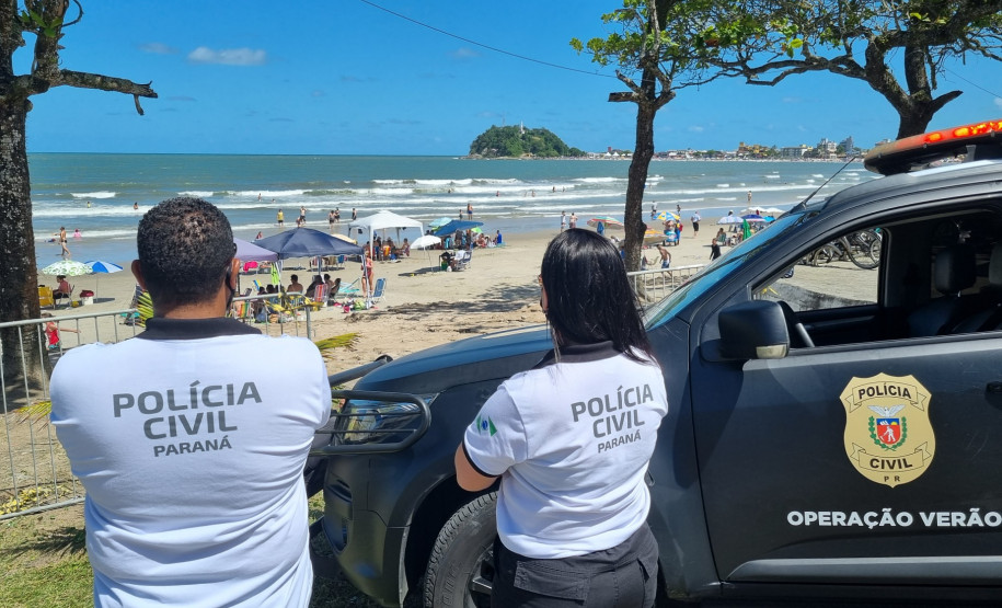 Dois policiais civis ao lado de viatura observam movimento na praia