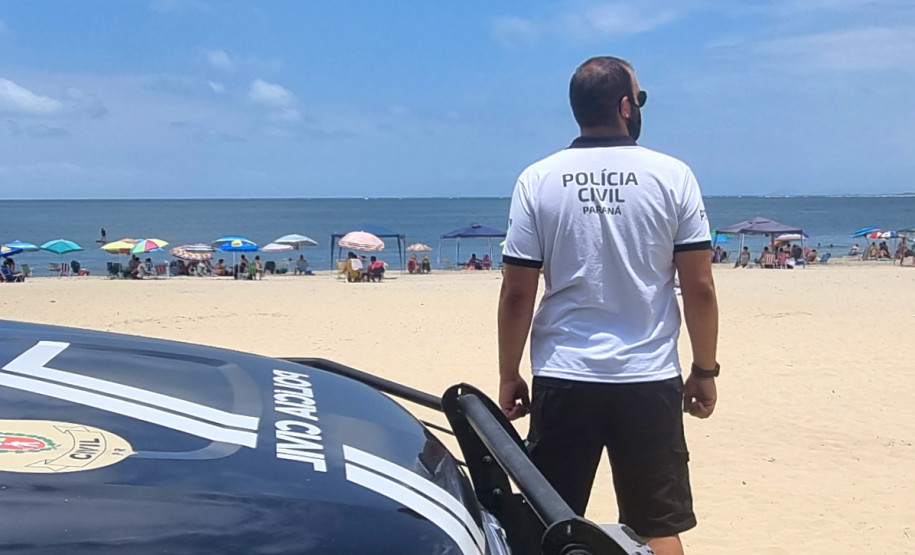 Policial civil ao lado de viatura observa veranistas