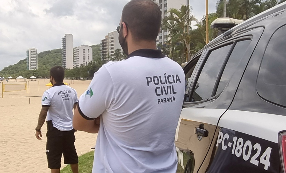Dois policiais civis ao lado de viatura observam veranistas