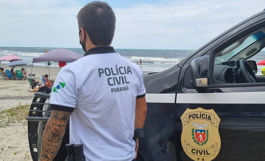 Policial civil ao lado de viatura observa veranistas