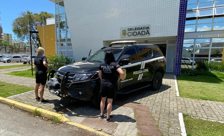 Duas policiais civis ao lado de viatura, em frente à delegacia de Matinhos