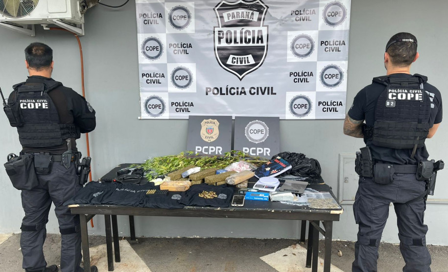 Dois policiais de costas ao lado de mesa com produtos apreendidos