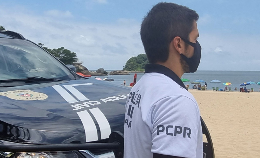 Policial civil ao lado de viatura observa veranistas