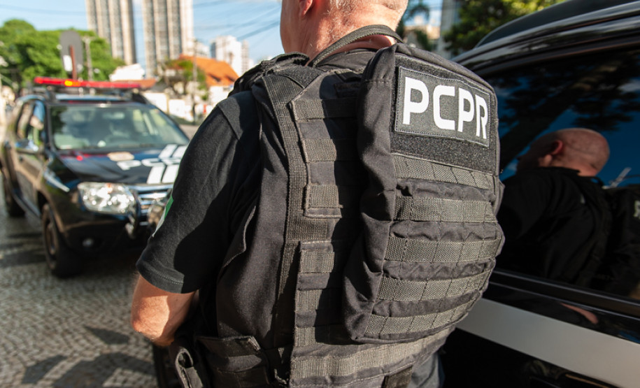 Policial civil de costas ao lado de viaturas