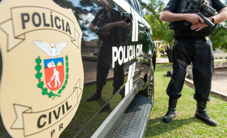 Policial civil empunha arma ao lado de viatura