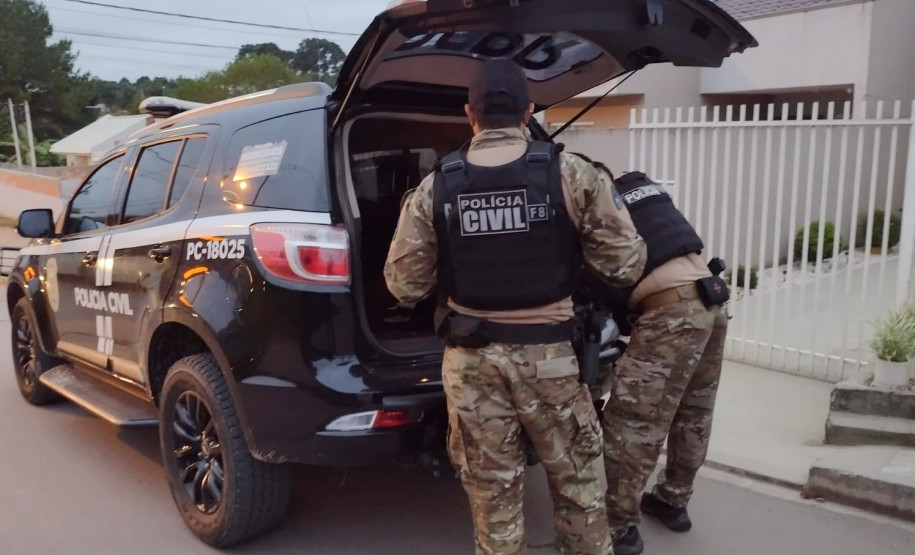 Dois policiais civis ao lado de viatura