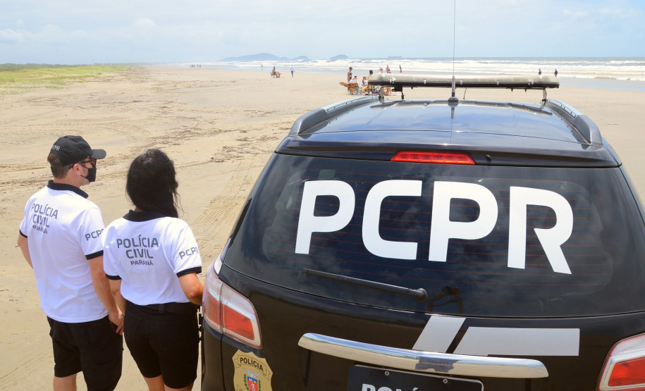 Dois policiais civis ao lado de viatura no litoral