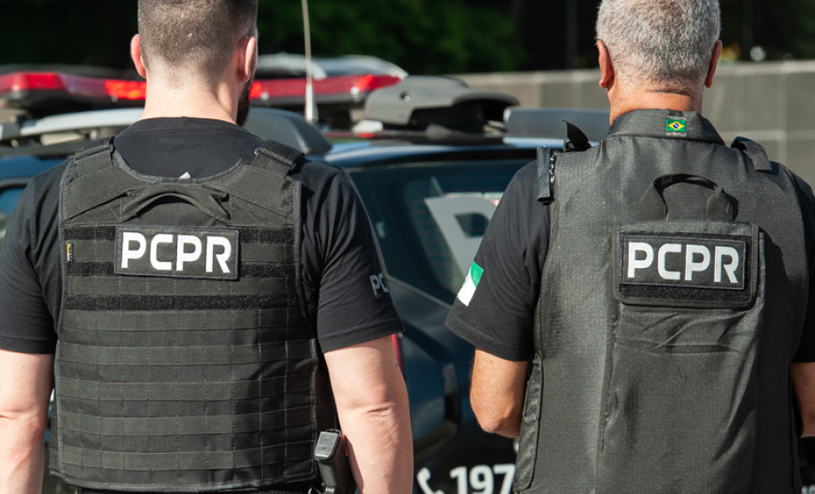 Dois policiais de costas ao lado de viatura