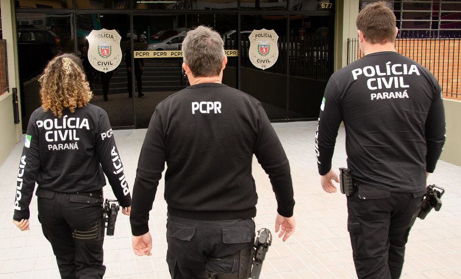 Três policiais de costas entrando em delegacia