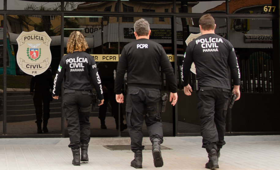 Tres policiais civis de costas entrando em delegacia
