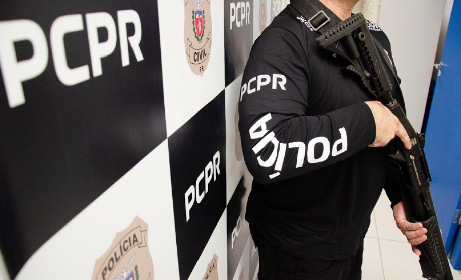 Policial civil empunhando arma ao lado de banner da PCPR