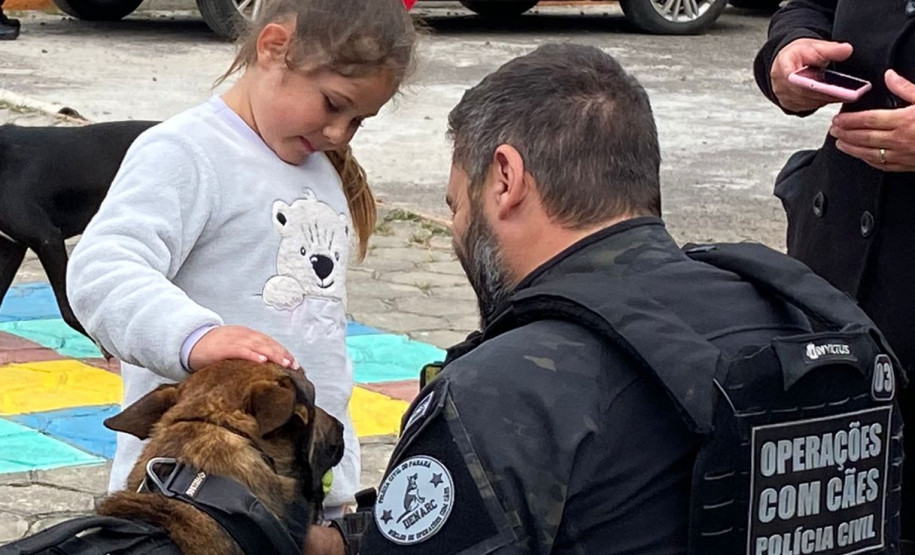 Policial civil acompanha criança acariciando cão policial