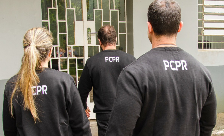 Três policiais civis de costas entrando em delegacia