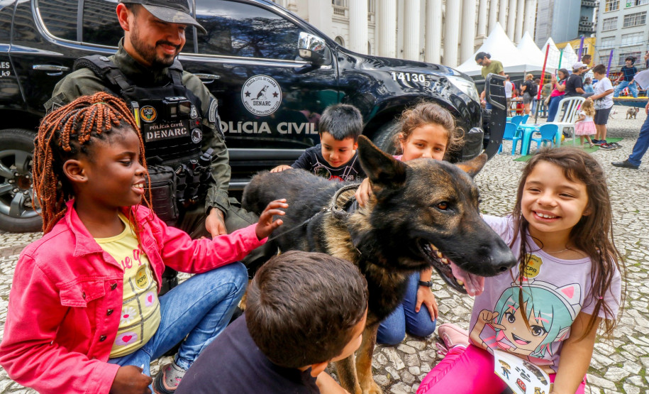 Policial civil observa crianças acariciando cão policial