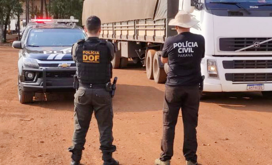 Dois policiais de costas observam caminhao com droga apreendida